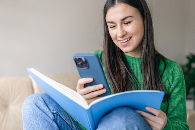 Joven opositora sonriente sosteniendo el móvil y un cuaderno mientras estudia con contenido en vídeo