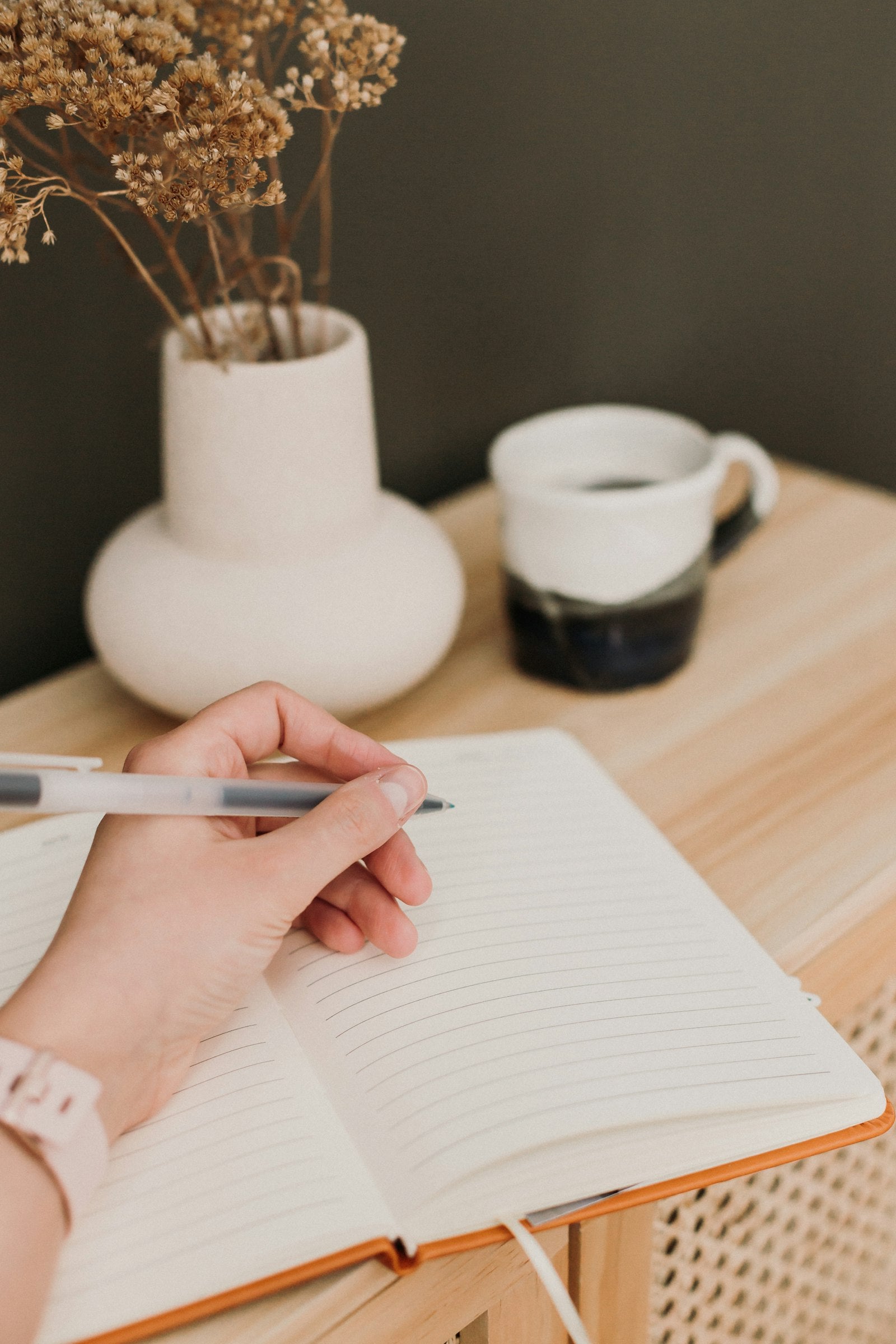 Persona escribiendo en un cuaderno de planificación con una taza de café al lado