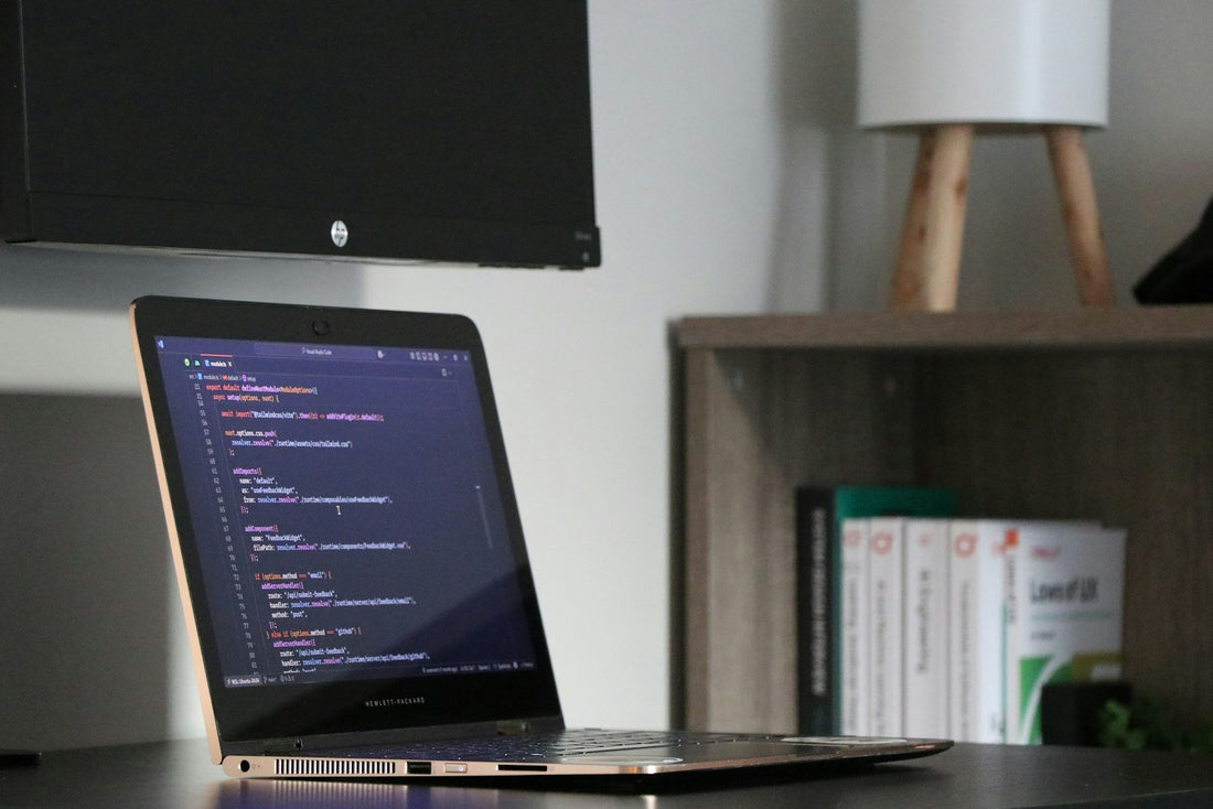 Portátil mostrando código en un escritorio con estantería de libros, representando el desarrollo de APIs