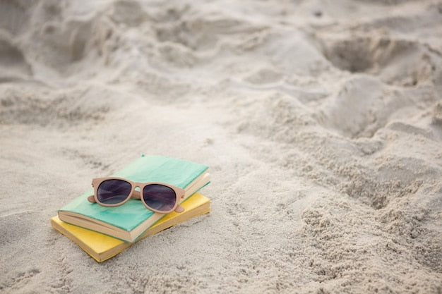 Gafas de sol y libros sobre la arena, representando los mitos de estudiar el TAI en verano